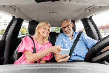 Happy senior couple having car trip together, using cell phone
