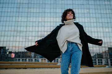 Young girl in jeans and knitted sweater spinning around in front of the building