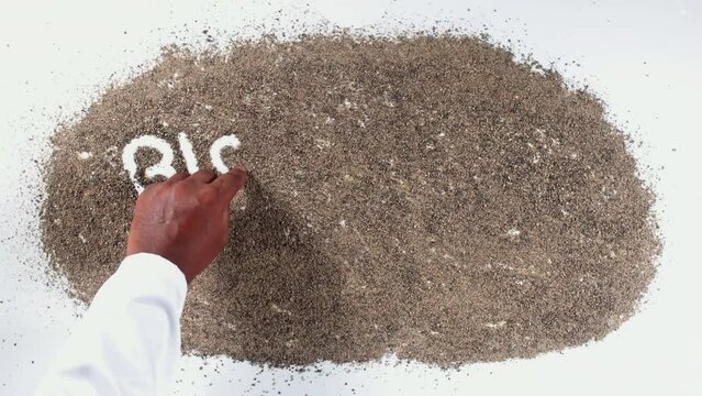 A hand of a person in a shirt writing on black sand words Black pepper