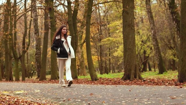 Slow motion, attractive pretty woman walking outdoor, young lady in warm sunny autumn park season, fall, yellow orange red leaves falling, smiling laughing giggle having fun 
