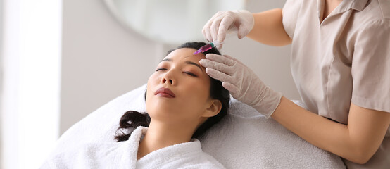 Fototapeta na wymiar Young Asian woman receiving injection in beauty salon. Skin care concept