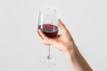 Female hand holding glass of red wine on grey background