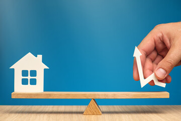 Rising property values. House model and arrow in hand pointing up. Scales as a symbol of the...