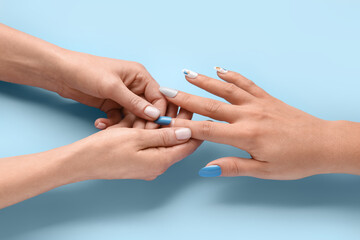 Manicure master applying press-on nail on blue background, closeup