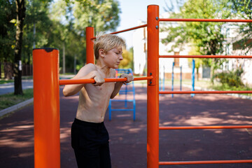 A fit child performed a sport pull-up on the bar. Street workout on a horizontal bar in the school park.