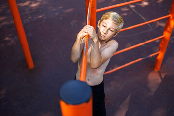 Sports child performs a side pull-up on the crossbar. Street workout on a horizontal bar in the school park.