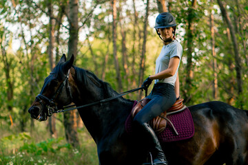 A rider dressed in a helmet rides her beautiful black horse in the forest during a horseback ride