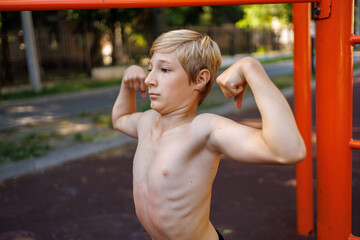 Obraz premium A teenager with an athletic build shows off his musculature. Street workout on a horizontal bar in the school park.