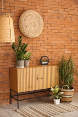 Stylish wooden cabinet with houseplants near brown brick wall