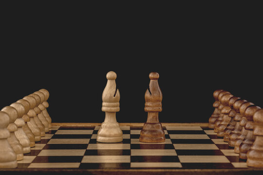 Concept of rivalry between teams and leaders. Two bishops, each with many pawns following, face off on the chessboard. Black background with copy space.