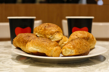 Delicious morning coffee for two: fresh buns on the background of paper cups on a table in a cafe, close-up