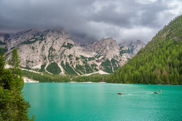 Braies lake surrounded by pine forests and the rocky ranges of the Dolomites in cloudy day, Italy.