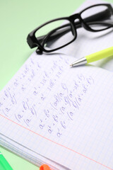 Copybook with maths formulas, glasses and pen on green background