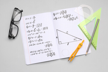 Copybook with maths formulas, glasses and stationery on grey background