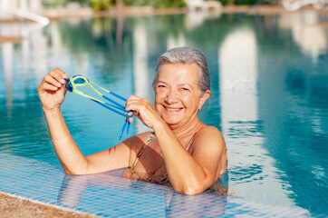 Happy active senior woman into the swimming pool with swimming googles in hands enjoying sport and...