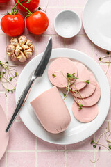 Composition with boiled sausage in plate, garlic and tomatoes on pink tile table © Pixel-Shot