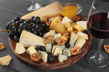 Plate with pieces of tasty cheese, grapes and honey on dark wooden background
