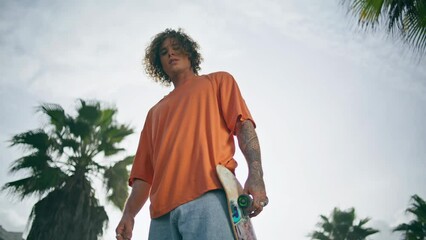 Stylish guy skateboarder standing street cloudy summer day with longboard.