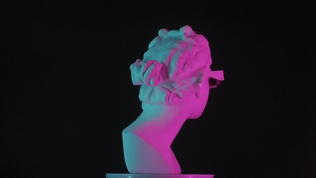 Closeup shot. Ancient marble bust statue of roman era woman in 3d glasses spinning round on a platform in neon lights. Isolated on black background. HDR BT2020 HLG Material.