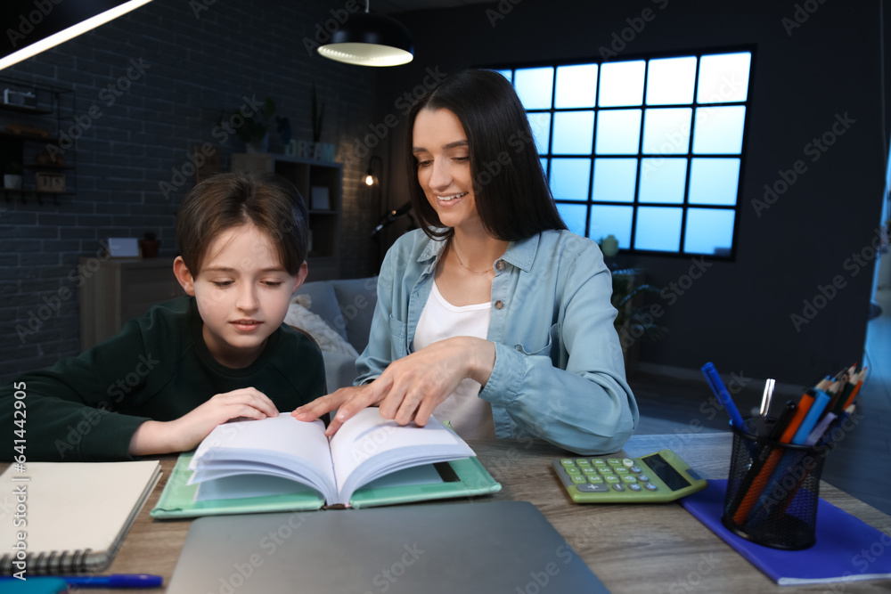 Wall mural mother with her little son sitting at table and reading book late in evening