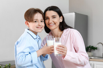 Little boy and his mother with glasses of fresh milk in kitchen