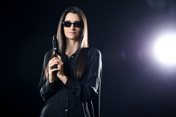 Stylish young woman in sunglasses with gun on black background