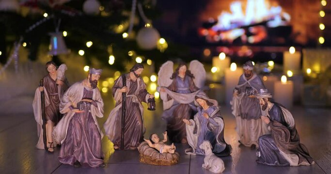 Jesus Christ Nativity scene in atmospheric lights near Christmas tree in front of fireplace. Christmas scene. Dolly shot 4k