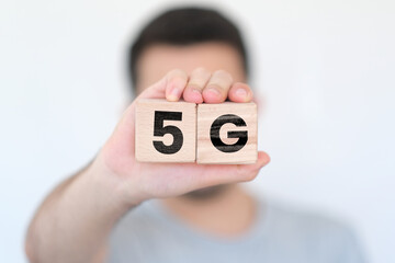 Man holding wooden cubes with 5G text on them, network or communication idea, wooden block cubes with 5G word, blurred man with wood blocks in front of white background, concept banner