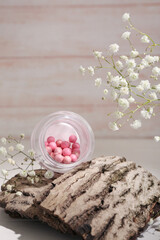 Jar of blush balls, tree bark and gypsophila flowers on light wooden table, closeup