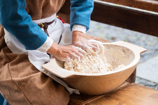 Woman dressed medieval costume sitting and kneading the fresh wheat dought. Healthy food and nutrition concept image.