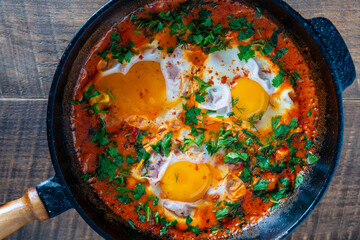 Delicious shakshuka with eggs, tomato and parsley in a cast-iron pan, closeup, top view. Shakshuka - traditional israeli tomato stew with eggs