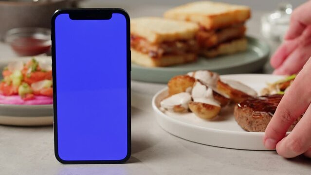 Fancy restaurant booking table application, delivery phone application with chroma key green screen, meals tar tar chicken and fried chicken french fries, on wooden table ready to takeaway. 
