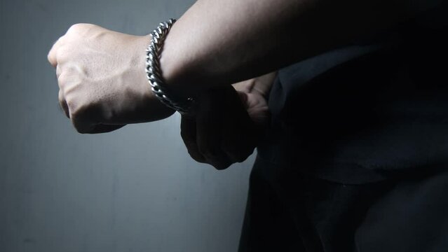 Fitting a large chain bracelet onto the wrist of an Asian man dressed in black. Attaching the bracelet clasp. Close-up of biker hands, motorcyclist with metal bracelets. 4K footage.