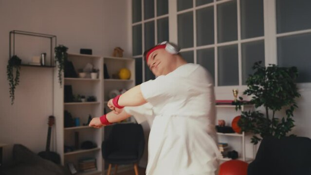 Young overweight man dancing in headphones at home, losing weight, activity