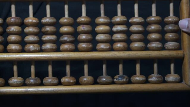 abacus. sempoa. Made of wood. Flipping over a wooden abacus with black background. 4K footage. Seeds following in the same direction, together and simultaneously.