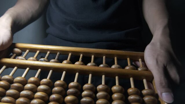 sempoa. Made of wood. A man of Asian descent is playing with an abacus by tossing and spinning the abacus frame. accounting, calculator, finance, mathematics, retro, traditional, computing.