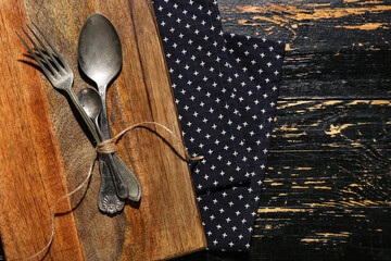New cutting board, spoons and fork on black wooden background