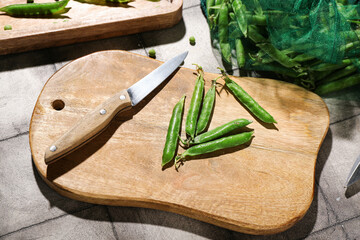 Wooden cutting board with green peas on grey tile background