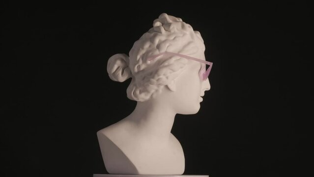 Closeup shot. Ancient marble bust statue of roman era woman in pink glasses spinning round on a platform. Isolated on black background. HDR BT2020 HLG Material.