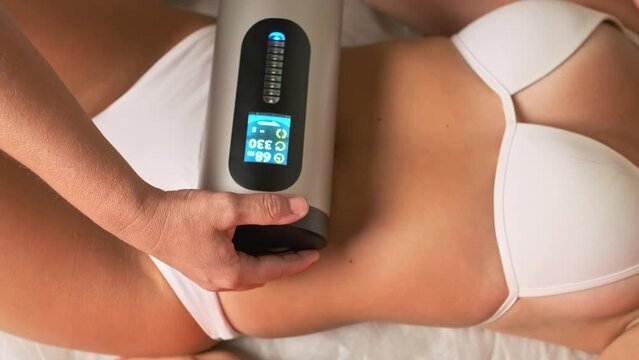 Spa worker massages woman client belly with cellulite remover. Appliance for smoothing skin relief and eliminating flabbiness in adulthood