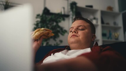 Closeup of overweight man eating junk food and using laptop, sedentary lifestyle