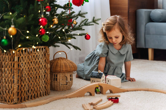 Child builds a toy town and  wooden railway. Christmas holidays. A little girl plays with toy train locomotive,  wooden blocks. Holiday Activity for Kids.