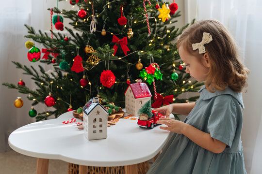 Christmas holidays. A little girl plays with toy cars, little houses and christmas decorations. Holiday Activity for Kids. Merry Christmas and Happy Holidays!