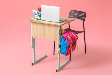 Modern school desk with backpack, laptop and stationery on pink background