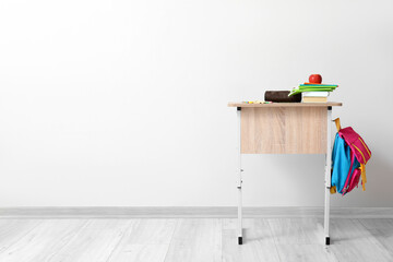 Modern school desk with backpack, fresh apple and stationery in room near white wall