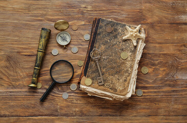Old manuscripts with spyglass, magnifier, compass and coins on brown wooden background