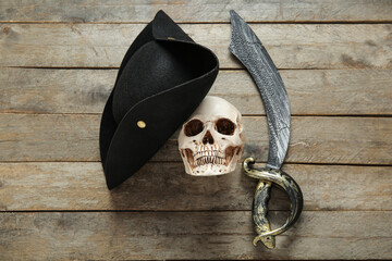 Human skull with pirate hat and sword on brown wooden background