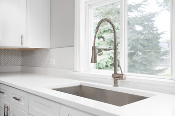 A kitchen faucet detail with a bronze faucet, white marble countertop, and a herringbone backsplash...