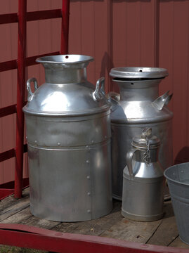 An outdoor setting shows off the old metal containers: milk cans, pitcher. A red wall highlights the shiny metal objects.