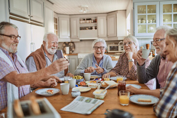 Group of senior friends having breakfast and using a smartphone in the morning in the kitchen